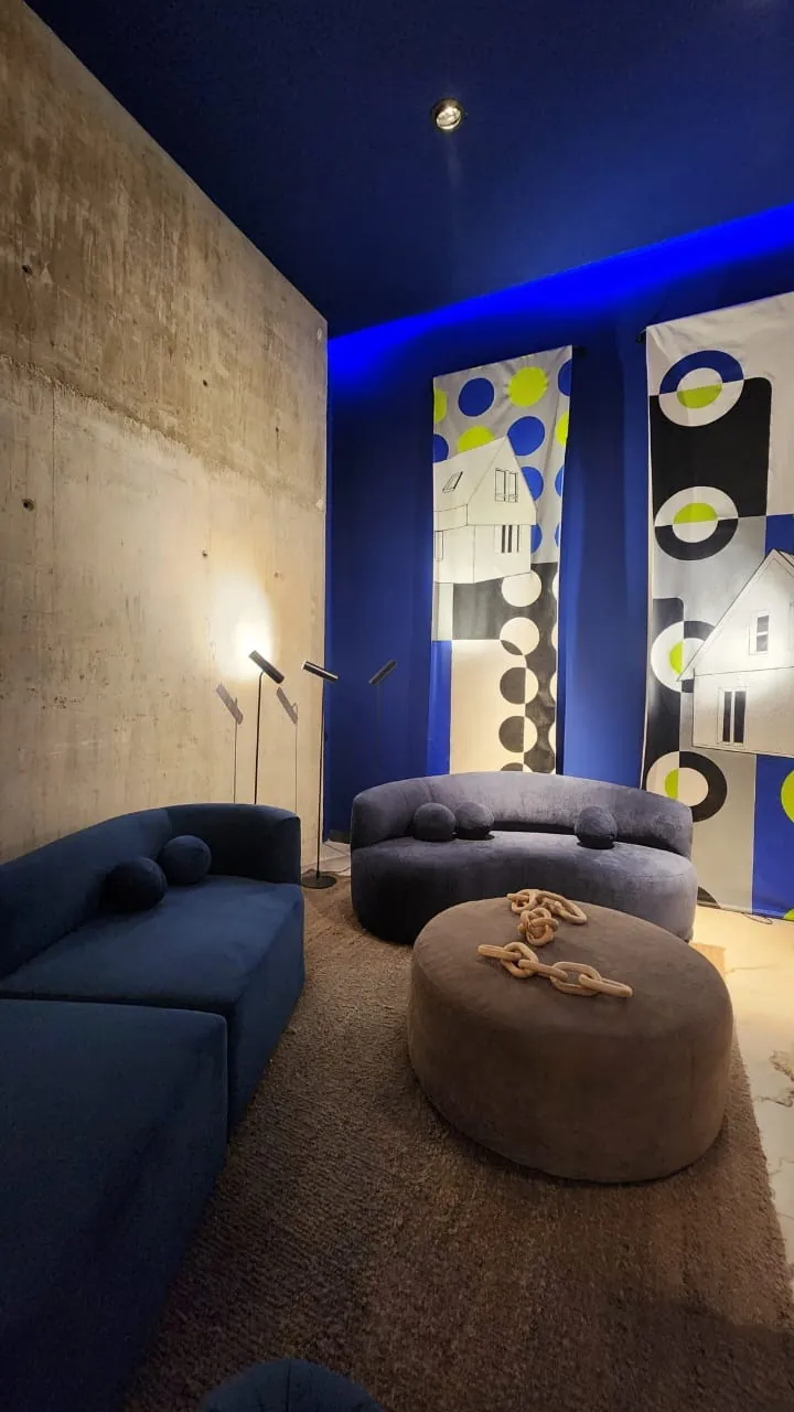 Maximalismo urbano: el color vuelve a ser protagonista (lo que vimos en Casa FOA 2025) Sala con techo y pared azul cobalto junto a una pared de hormigón visto y sillones azules