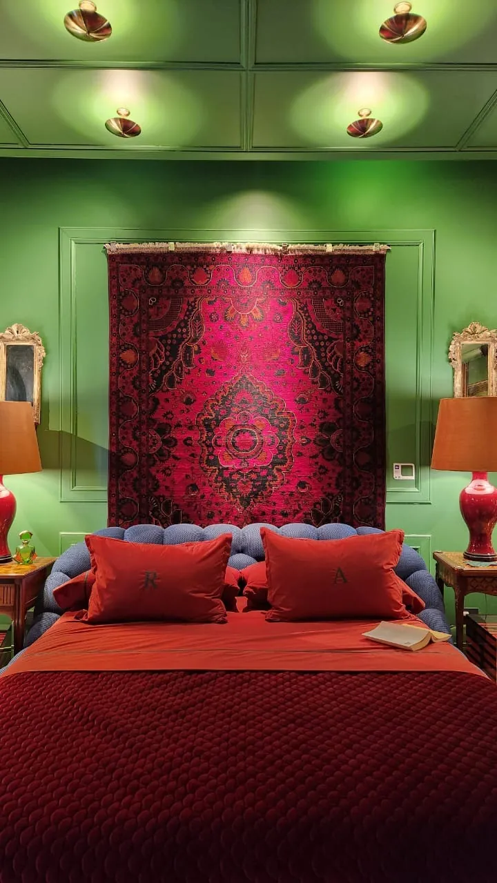 Maximalismo urbano: el color vuelve a ser protagonista (lo que vimos en Casa FOA 2025) Dormitorio con paredes verdes, tapiz rojo sobre el cabezal y ropa de cama roja