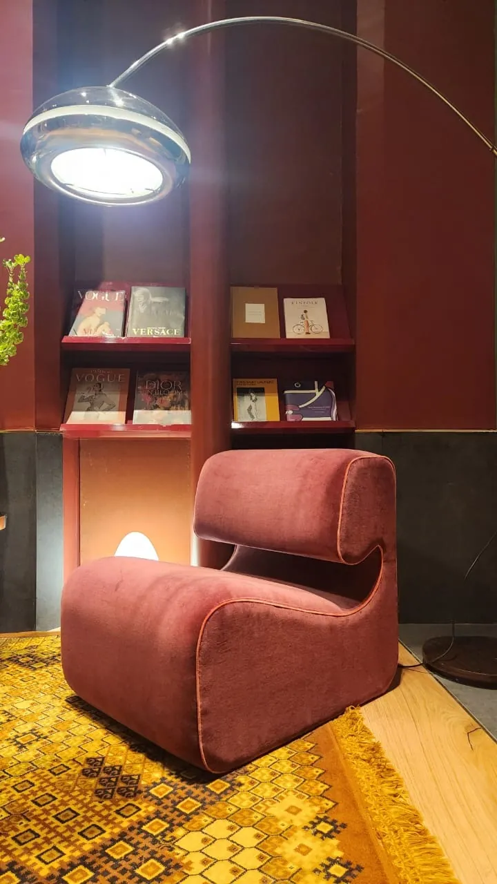 Maximalismo urbano: el color vuelve a ser protagonista (lo que vimos en Casa FOA 2025) Rincón con sillón bordó, lámpara de arco, alfombra amarilla y estantes con libros sobre pared roja