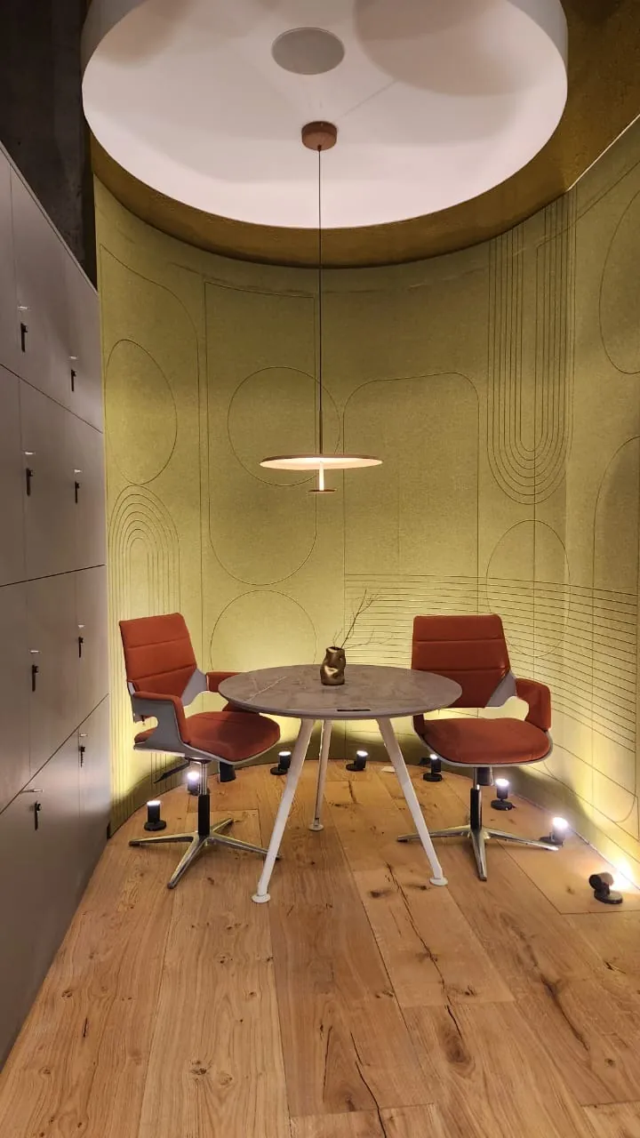 Maximalismo urbano: el color vuelve a ser protagonista (lo que vimos en Casa FOA 2025) Sala de reuniones circular con pared verde, mesa redonda y sillas color óxido